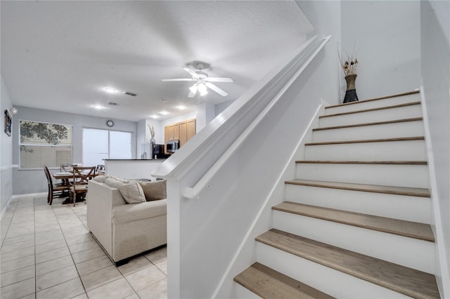 staircase featuring tile patterned floors, ceiling fan, and a textured ceiling