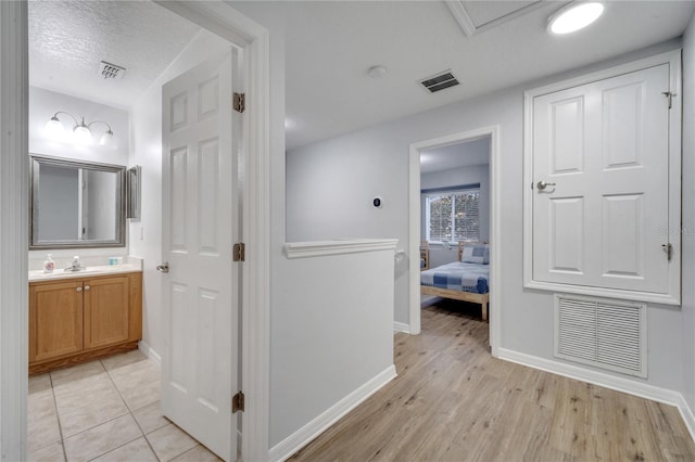 corridor with a textured ceiling, light wood-type flooring, and sink