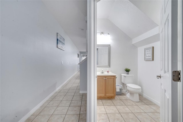 bathroom featuring toilet, tile patterned floors, vanity, and vaulted ceiling