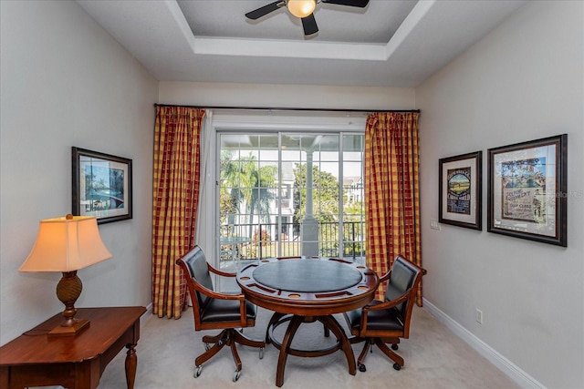 dining area featuring light carpet, a raised ceiling, and ceiling fan