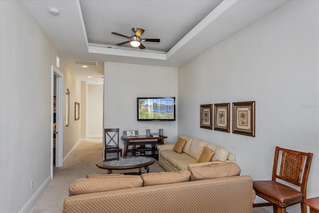 living room featuring light carpet, a tray ceiling, and ceiling fan