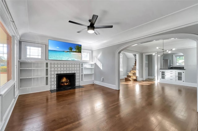 unfurnished living room with ceiling fan, ornamental molding, wood-type flooring, and built in shelves