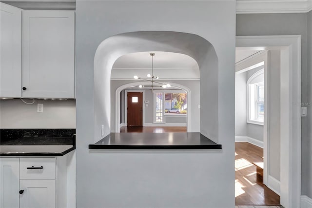 kitchen featuring hardwood / wood-style floors, white cabinetry, a healthy amount of sunlight, ornamental molding, and a chandelier