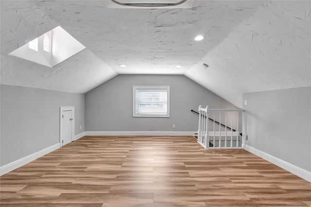 additional living space featuring a textured ceiling, lofted ceiling, and light wood-type flooring