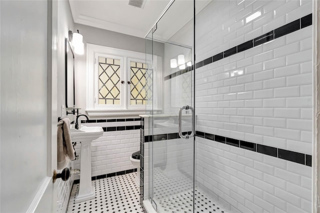 bathroom with toilet, crown molding, a shower with shower door, and tile walls