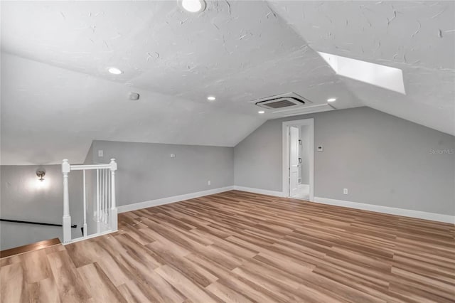 bonus room with lofted ceiling with skylight and light wood-type flooring