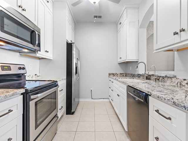 kitchen with white cabinets, sink, light stone countertops, light tile patterned flooring, and stainless steel appliances