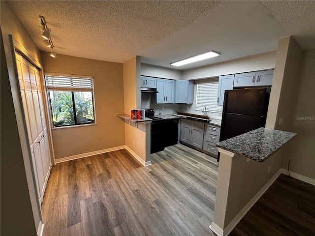 kitchen featuring kitchen peninsula, light stone countertops, a textured ceiling, black appliances, and light hardwood / wood-style floors