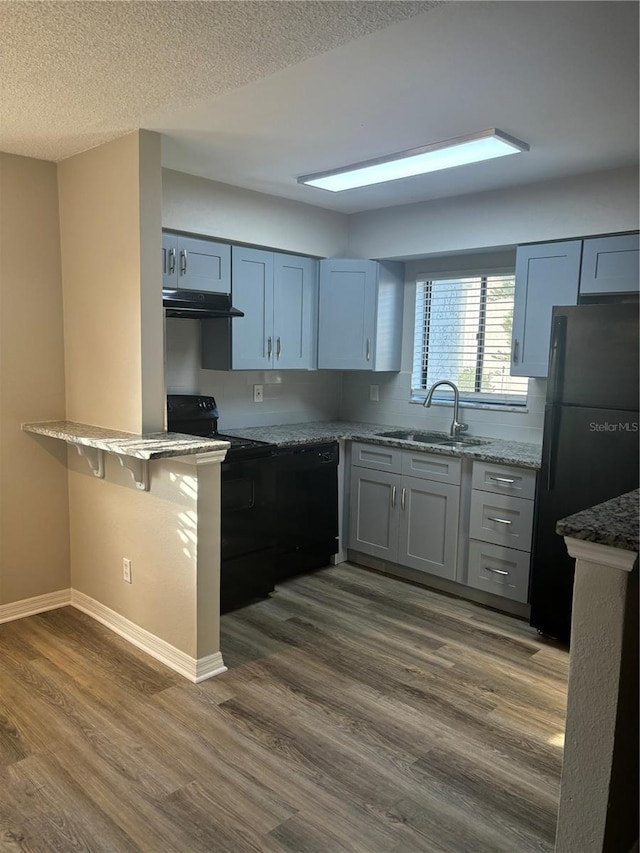 kitchen featuring light stone countertops, black appliances, dark hardwood / wood-style floors, and sink