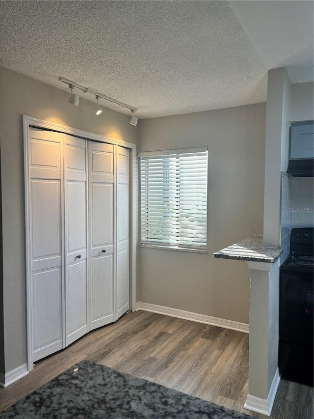 interior space featuring wood-type flooring, track lighting, black electric range, and a textured ceiling