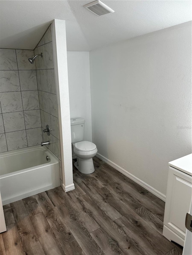 full bathroom featuring hardwood / wood-style floors, vanity, tiled shower / bath, toilet, and a textured ceiling