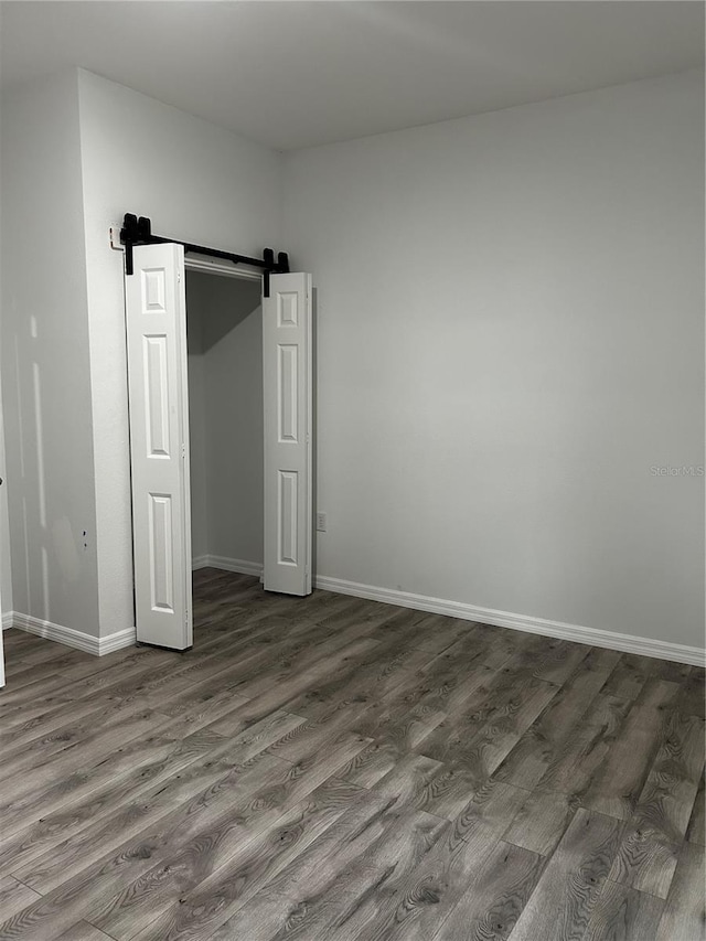 unfurnished bedroom featuring a barn door, a closet, and dark wood-type flooring