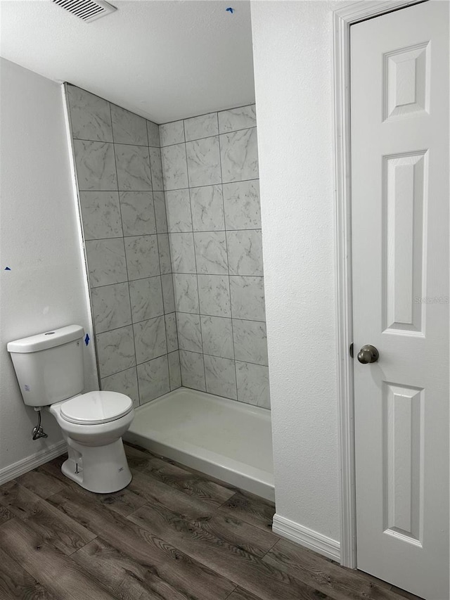 bathroom featuring a tile shower, hardwood / wood-style floors, and toilet