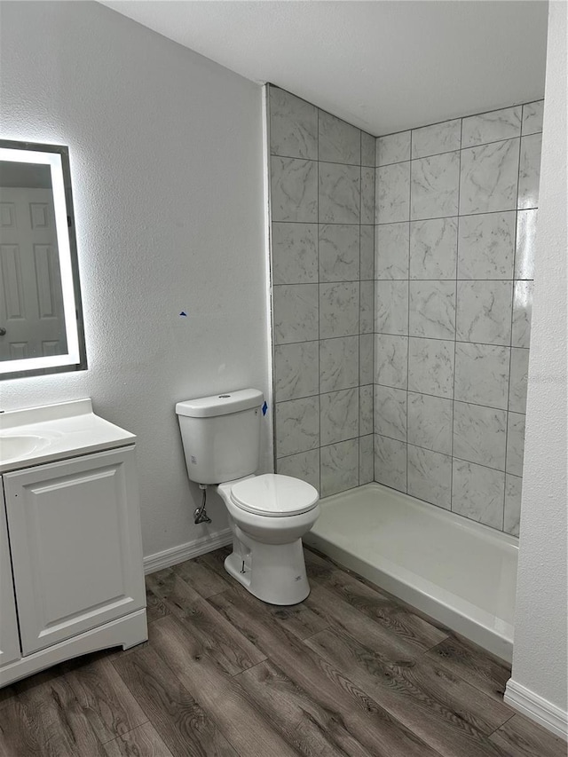 bathroom featuring a tile shower, vanity, wood-type flooring, and toilet