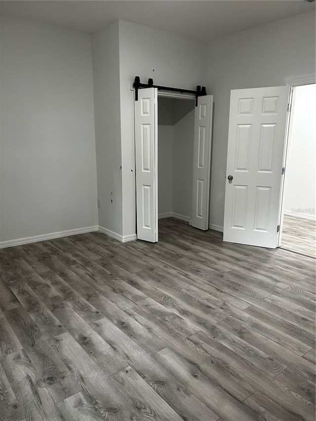 unfurnished bedroom with wood-type flooring, a barn door, and a closet