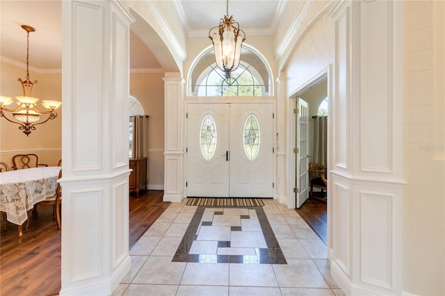 foyer featuring decorative columns, crown molding, a chandelier, and light hardwood / wood-style floors