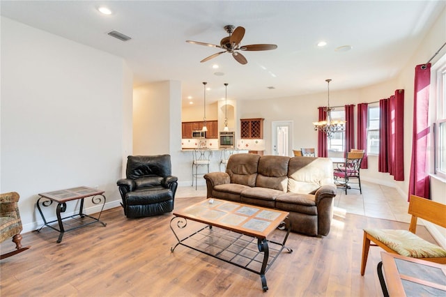 living room with light hardwood / wood-style floors and ceiling fan with notable chandelier