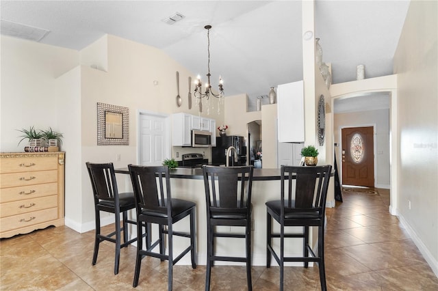 kitchen with stainless steel appliances, high vaulted ceiling, an inviting chandelier, white cabinetry, and a breakfast bar area