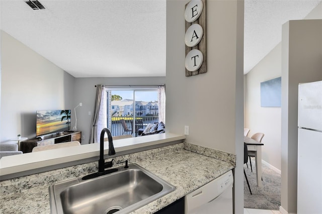 kitchen with a textured ceiling, white appliances, lofted ceiling, and sink