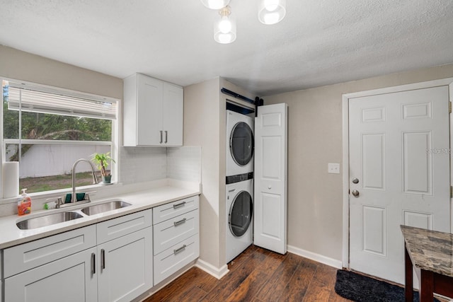 washroom with a textured ceiling, stacked washing maching and dryer, dark hardwood / wood-style floors, and sink