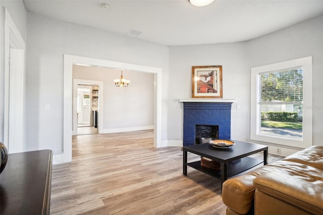 living room with light hardwood / wood-style flooring, an inviting chandelier, and a brick fireplace