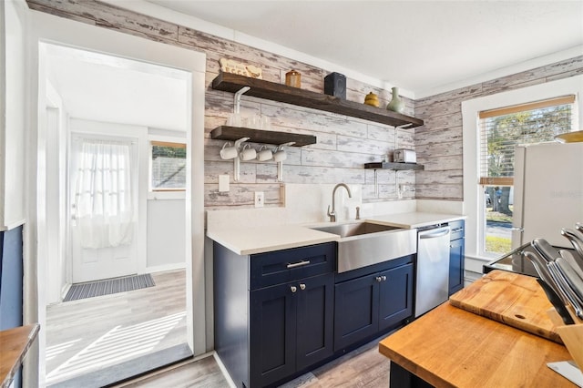 kitchen with stainless steel dishwasher, blue cabinets, sink, light hardwood / wood-style flooring, and white fridge