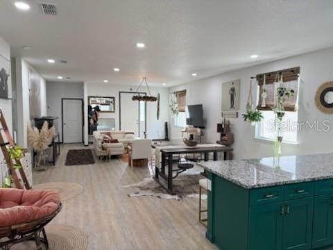 kitchen with a center island, green cabinets, light stone counters, light hardwood / wood-style flooring, and a breakfast bar