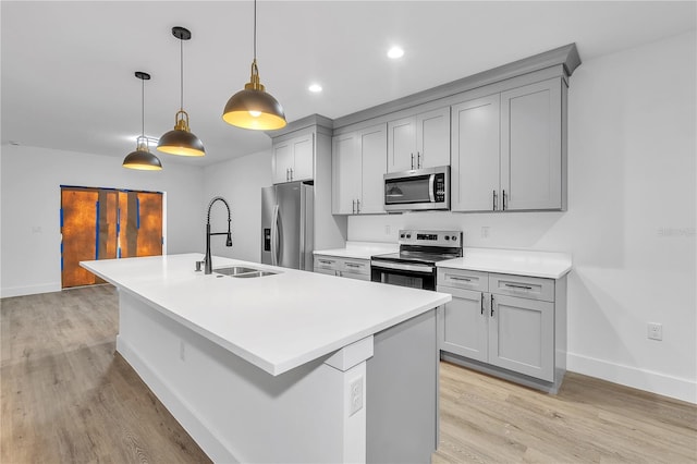 kitchen featuring decorative light fixtures, light wood-type flooring, a kitchen island with sink, and appliances with stainless steel finishes