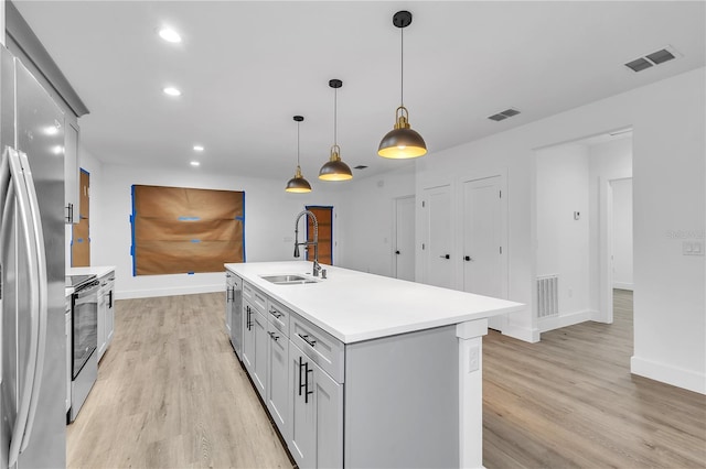 kitchen featuring pendant lighting, a kitchen island with sink, sink, appliances with stainless steel finishes, and light hardwood / wood-style floors