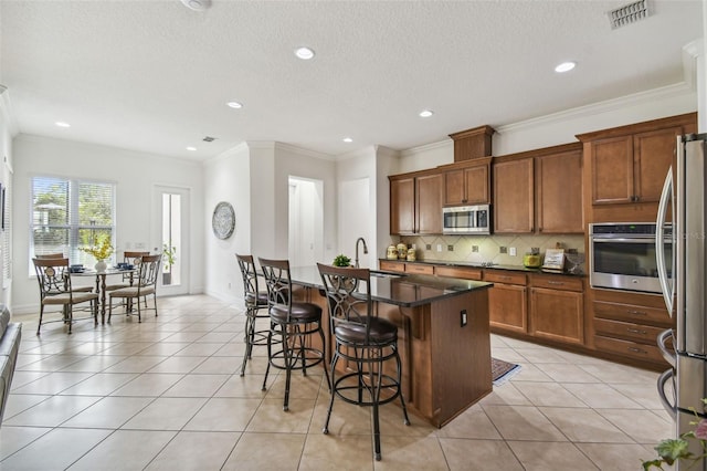 kitchen featuring tasteful backsplash, an island with sink, a breakfast bar, light tile patterned floors, and appliances with stainless steel finishes