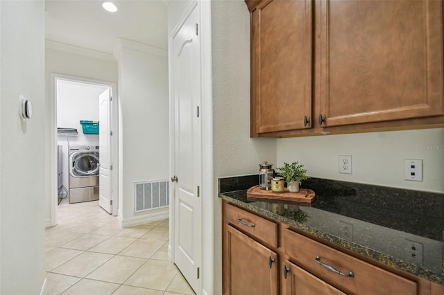 kitchen with washer and dryer, light tile patterned floors, crown molding, and dark stone counters