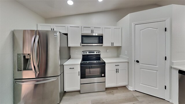 kitchen with light hardwood / wood-style flooring, white cabinets, stainless steel appliances, and lofted ceiling