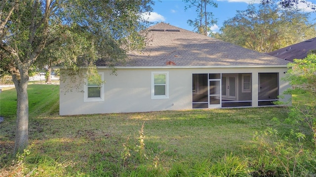 rear view of property with a sunroom, roof with shingles, a yard, and stucco siding