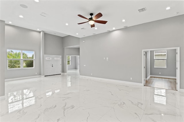 unfurnished living room featuring a high ceiling, ceiling fan, and a healthy amount of sunlight