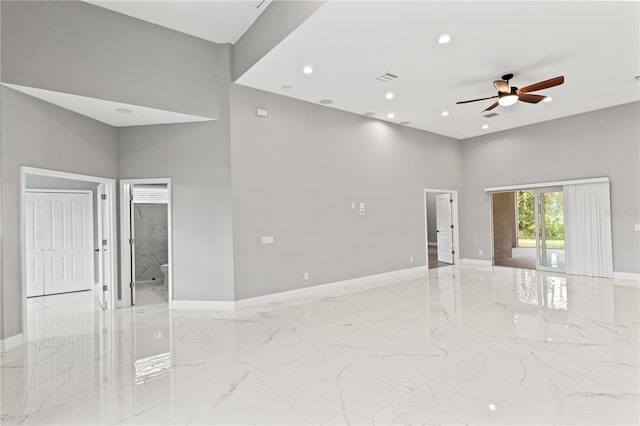 empty room with marble finish floor, a high ceiling, recessed lighting, and baseboards