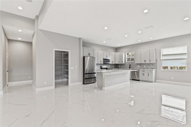 kitchen featuring marble finish floor, stainless steel appliances, light countertops, decorative backsplash, and a kitchen island