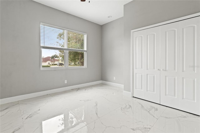 unfurnished bedroom with marble finish floor, baseboards, and a closet