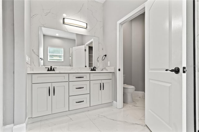 full bath featuring marble finish floor, double vanity, a sink, and toilet