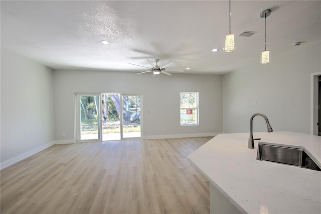 kitchen featuring pendant lighting, sink, light hardwood / wood-style floors, light stone countertops, and a textured ceiling