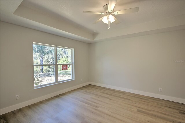 unfurnished room with ceiling fan, a raised ceiling, and light hardwood / wood-style floors