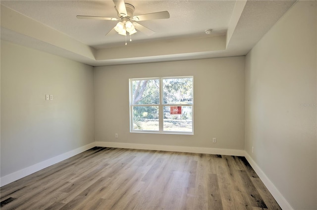 spare room with a raised ceiling, ceiling fan, and light wood-type flooring