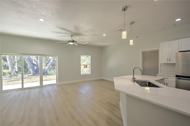 kitchen with sink, stainless steel refrigerator, pendant lighting, light stone countertops, and white cabinets