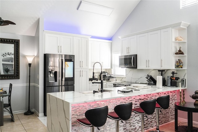 kitchen with kitchen peninsula, appliances with stainless steel finishes, vaulted ceiling, sink, and white cabinetry