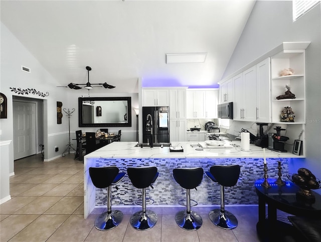 kitchen featuring light tile patterned floors, a kitchen breakfast bar, kitchen peninsula, black refrigerator, and white cabinets