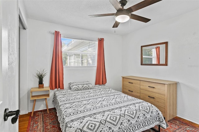 bedroom with a textured ceiling, ceiling fan, and dark wood-type flooring