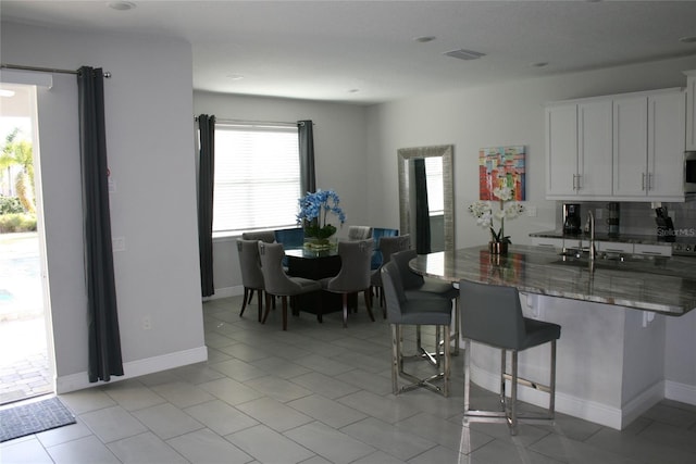 kitchen featuring white cabinetry, sink, a kitchen breakfast bar, dark stone counters, and decorative backsplash