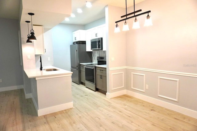 kitchen featuring appliances with stainless steel finishes, sink, decorative light fixtures, light hardwood / wood-style flooring, and white cabinets