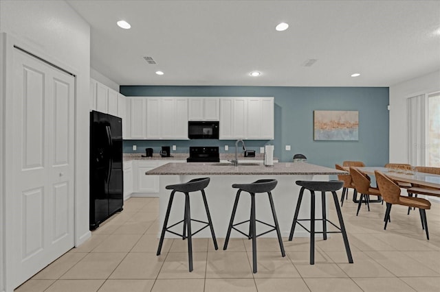 kitchen featuring a kitchen island with sink, sink, white cabinets, and black appliances