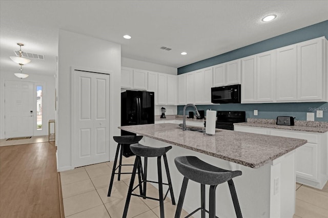 kitchen with light tile patterned floors, white cabinetry, a kitchen island with sink, and black appliances