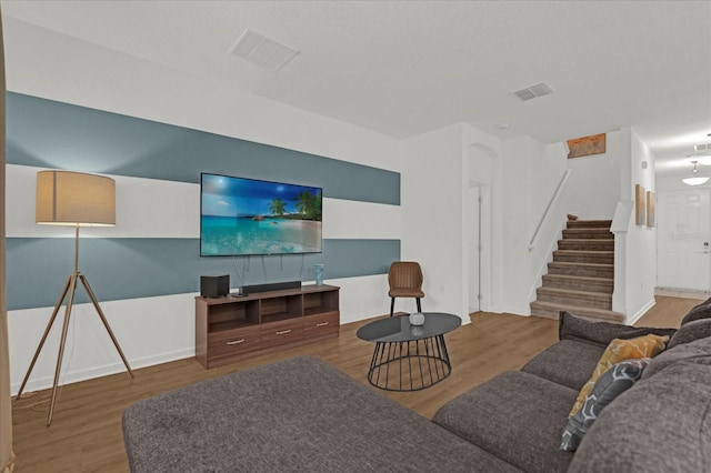 living room with visible vents, baseboards, wood finished floors, and stairway